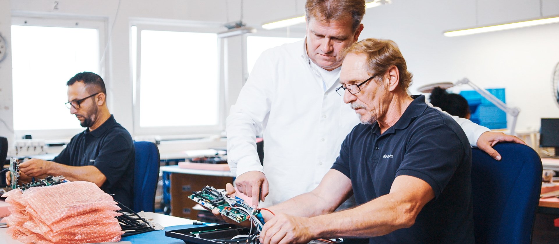 Aufnahme von drei Personen, welche bei der Arbeit sind. Eine Person erklärt der anderen etwas